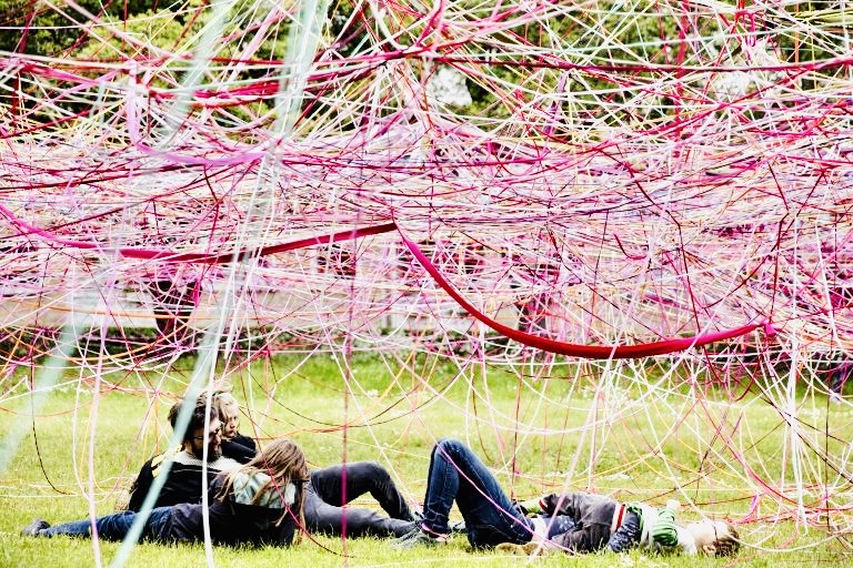 Friends laying under a pink string canopy on the grass